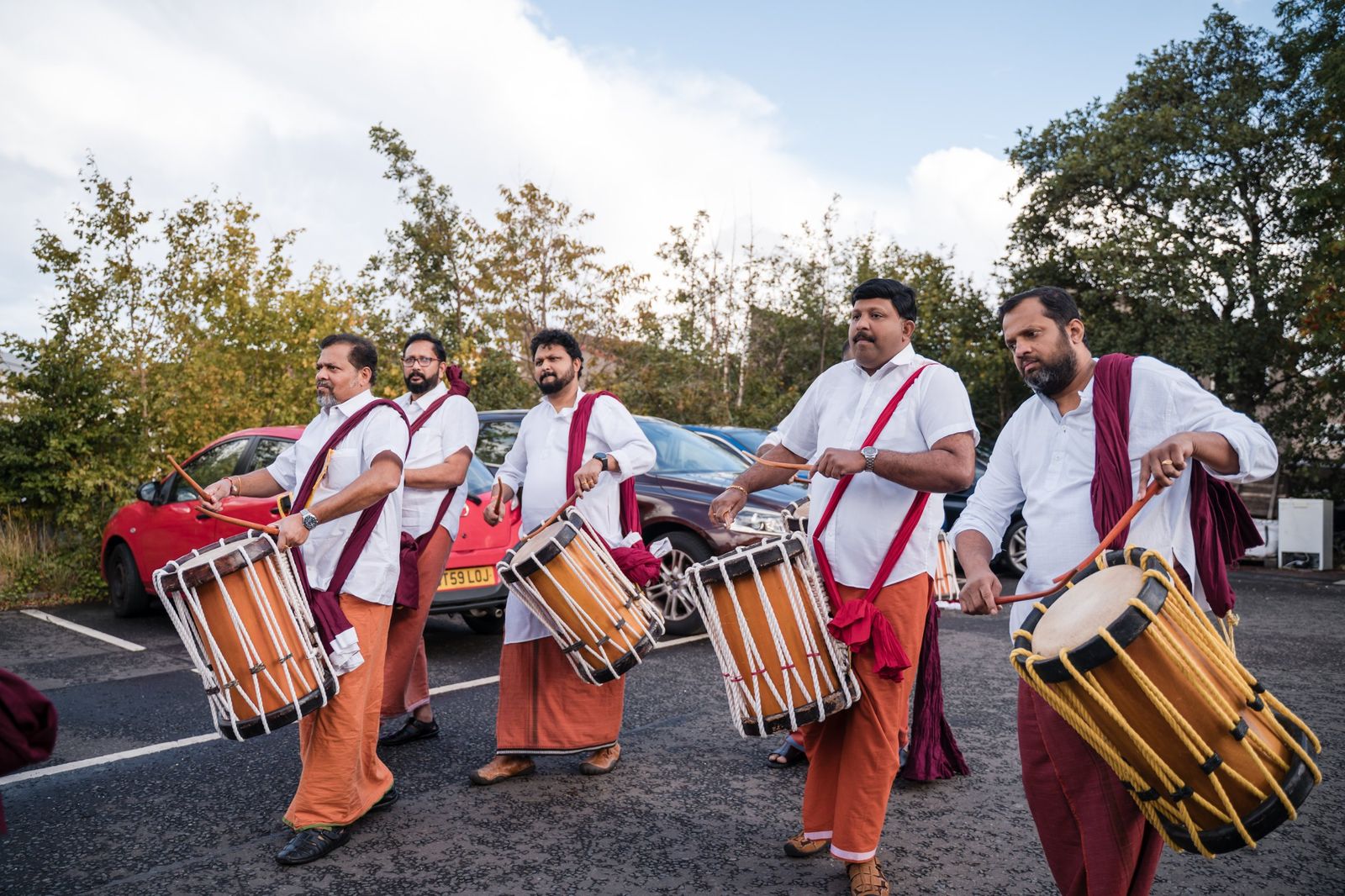 Chenda melam drummers in white shirts and orange mundu marching