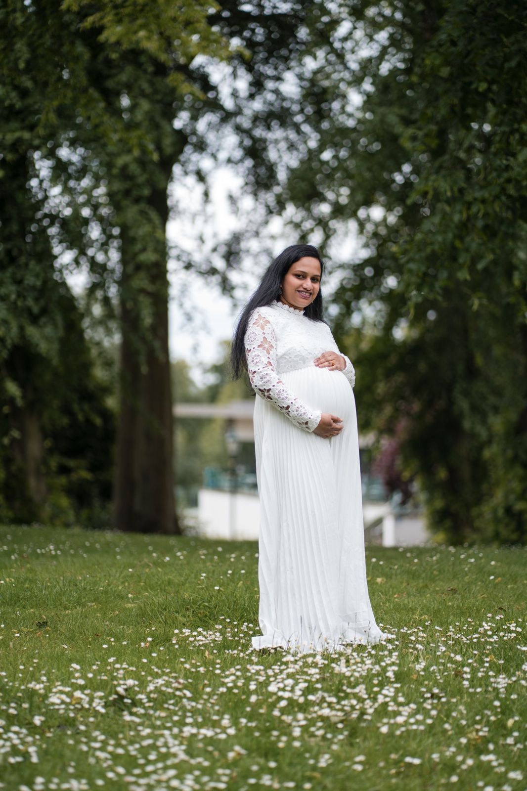 Mother-to-be in a white lace dress standing among daisies