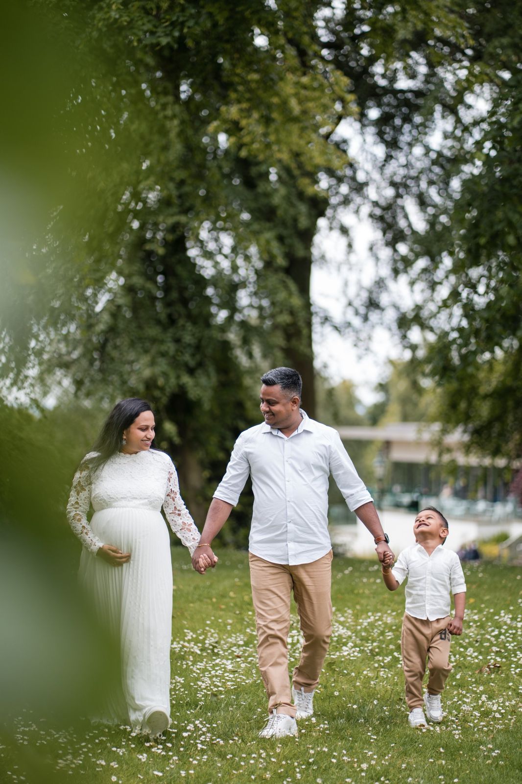 Expecting couple and their son walking hand in hand through a park